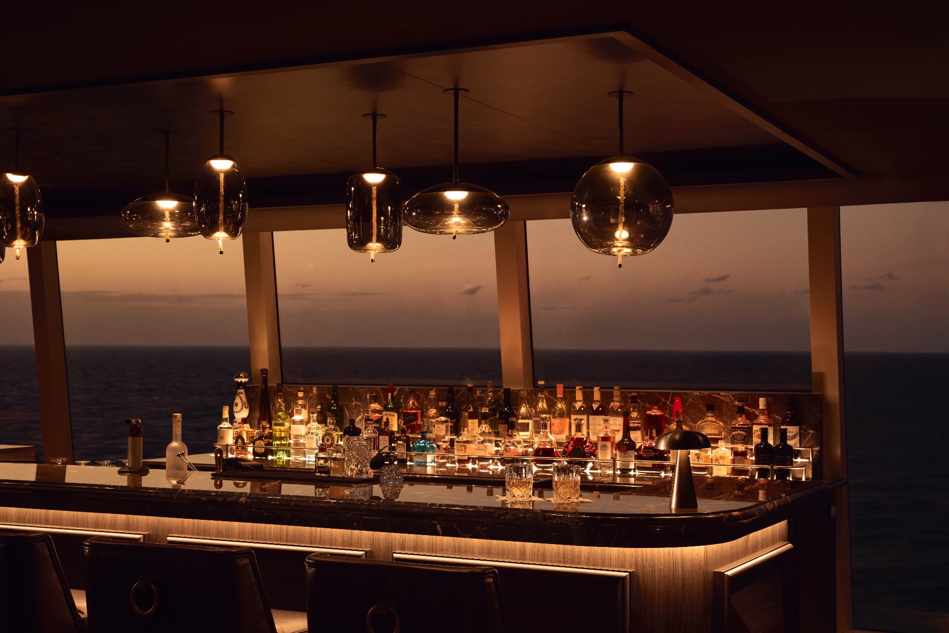 The Malt Whisky Bar on Explora II at dusk, bottles lit above a marble bar facing the sea